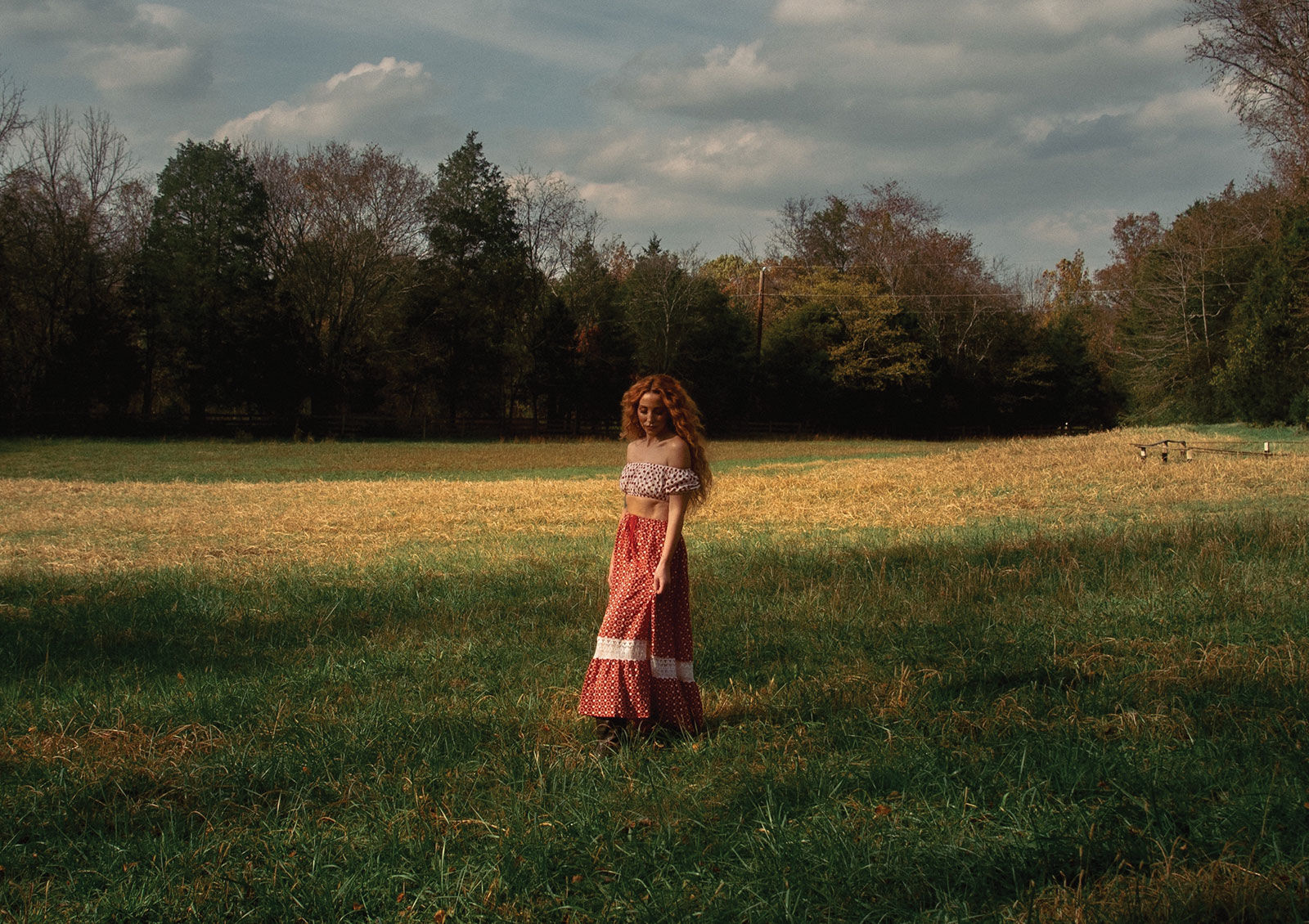 Press photo 2025 Ashley Monroe wearing a rose colored dress stands in a field looking down